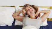 Woman laying down in her bed stretching as she wakes up